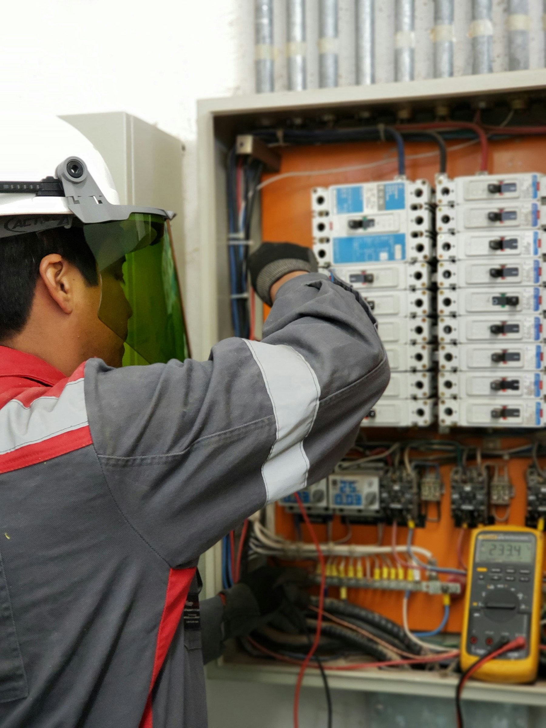 Electrician in a face shield testing an electrical panel